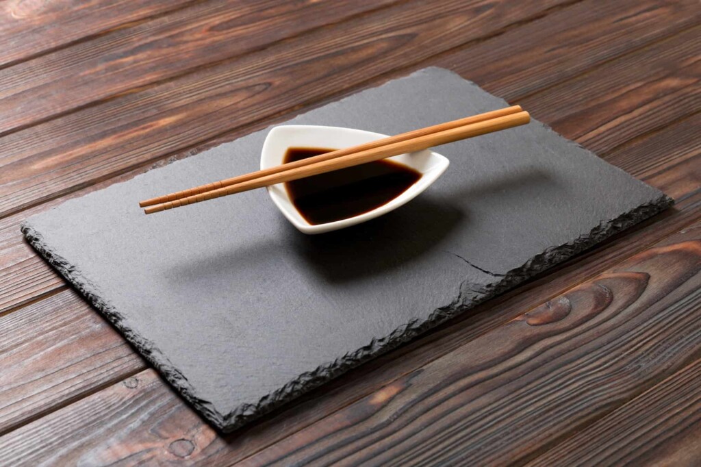 Chopsticks and soy sauce on black stone plate, wooden background