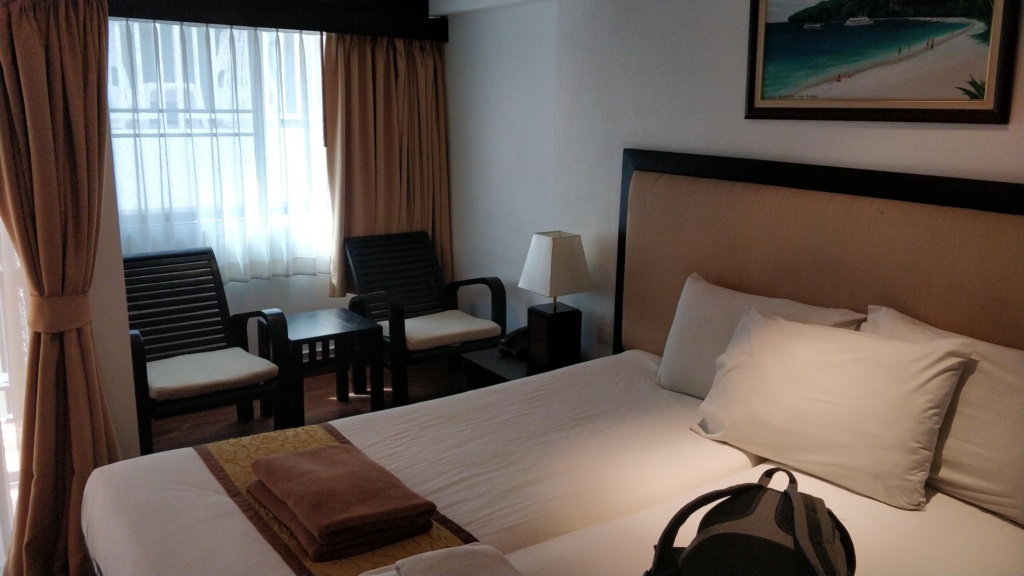 a hotel room in Krabi with 2 chairs and two single beds. Painting on the wal